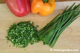 Chives that are partially finely chopped on a cutting board with a red and a yellow pepper - Renee's Garden