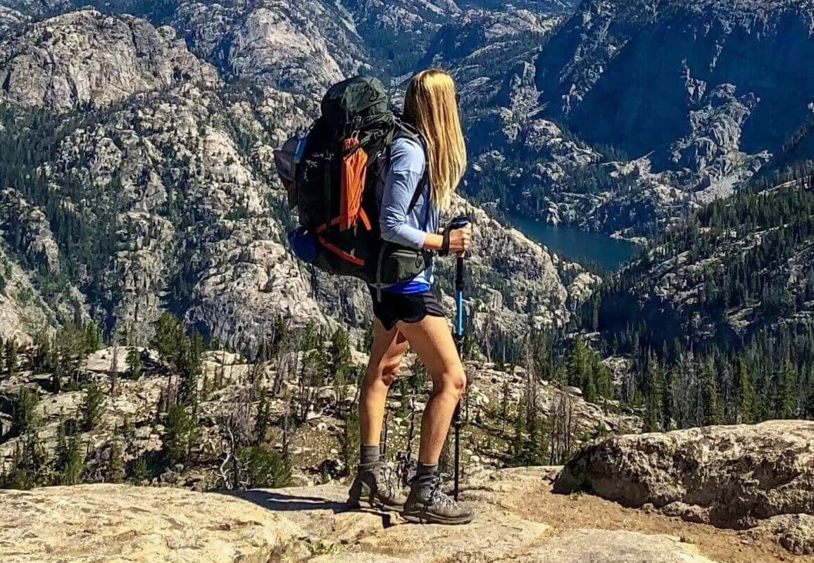 A woman hiker standing on top f a mountain with a hiking staff in her hand.