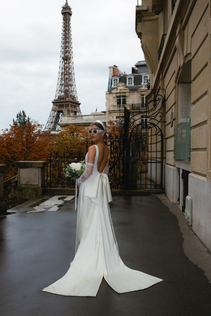 Bride stands in front of the Eiffel Tower in a long white bridal gown with a flared train