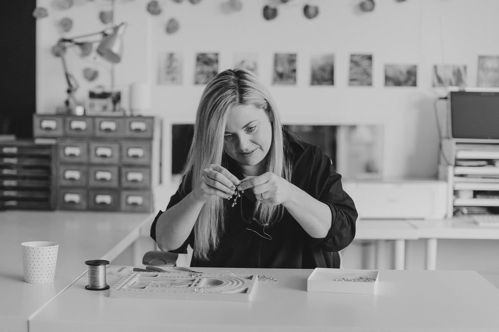 Debbie Carlisle sits at her making table handwiring a hair accessory using her artisan skills
