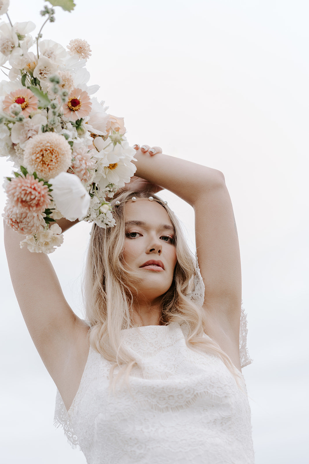 Bride with peachy white bouquet held above her head and gold pearl headband