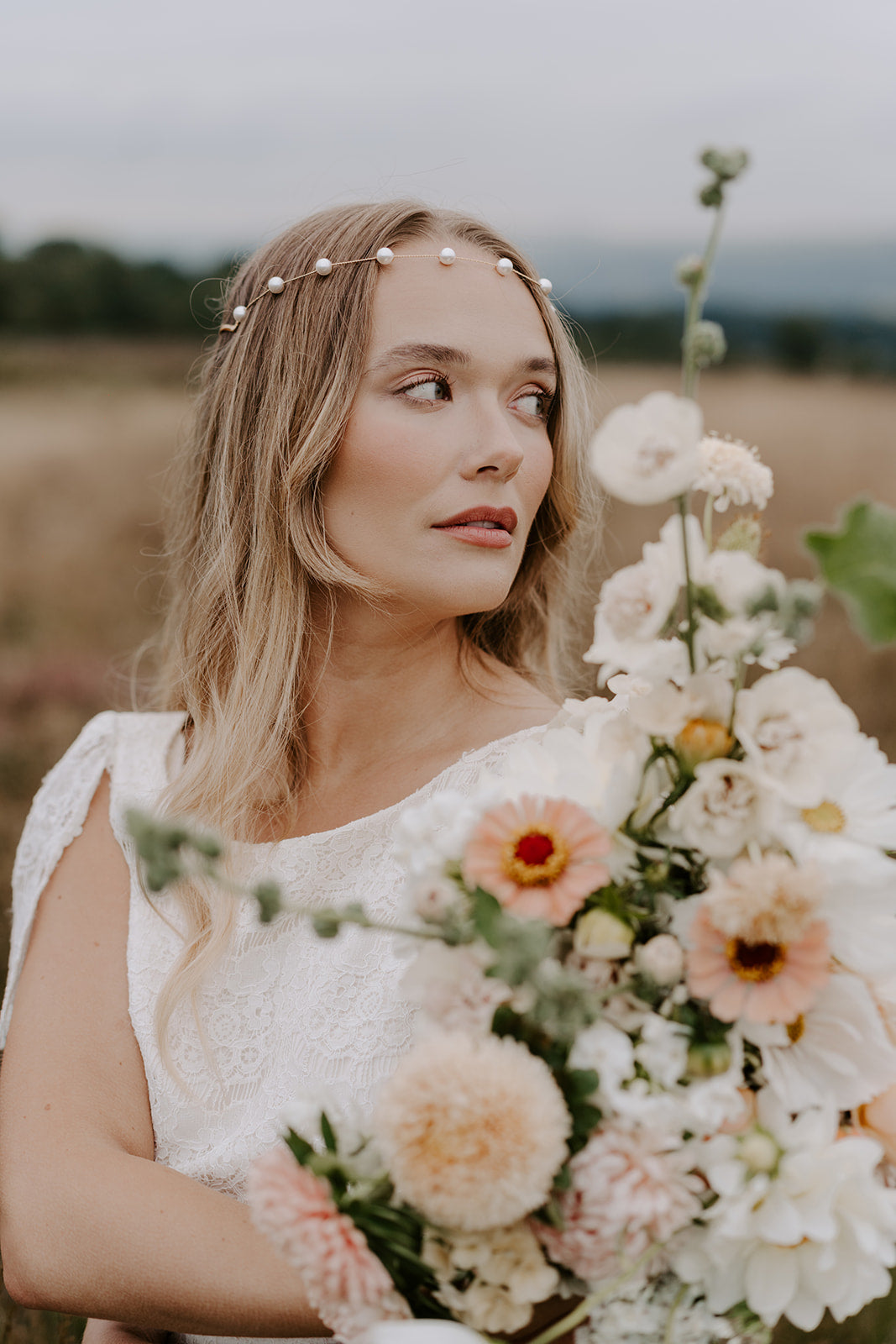 Bride with peachy floral bouquet wears simple pearl forehead in the countryside