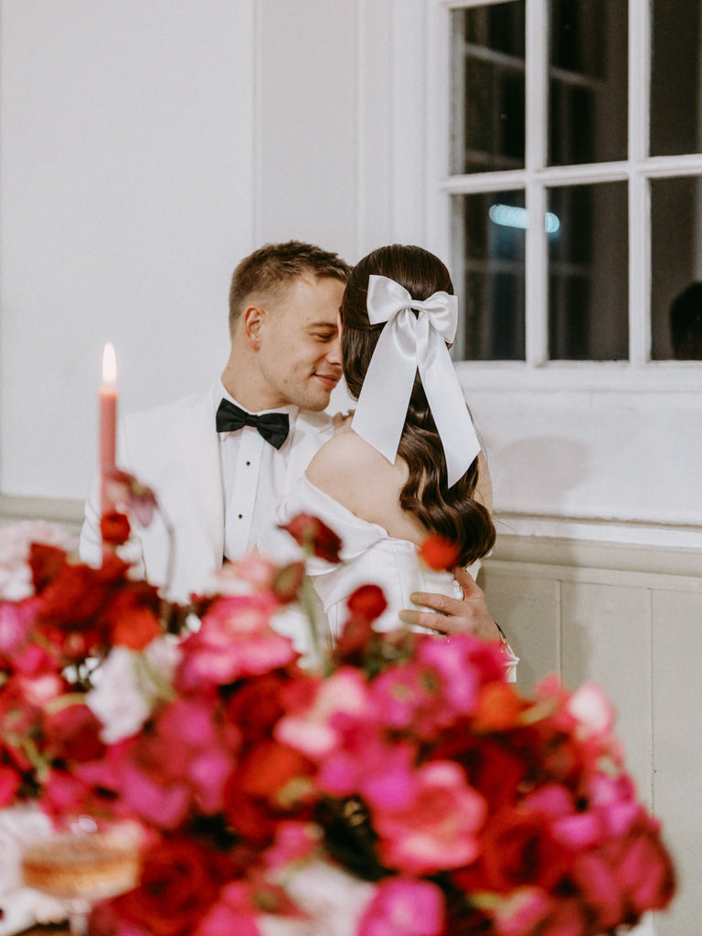 A white satin hair bow for a modern romantic bride and groom with colour pop pink and red flowers