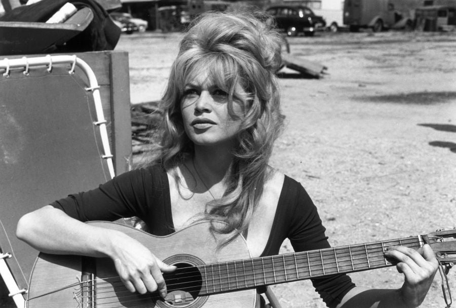 Brigitte Bardot circa 1960: French actor Brigitte Bardot playing guitar while sitting on a lawn chair in an empty lot. (Photo by Hulton Archive/Getty Images)