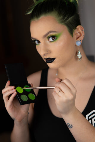 Alt Model Naomi wearing the Killin it Cemetery palette green eyeshadow and Nightshade black lipstick holding the palette and brush