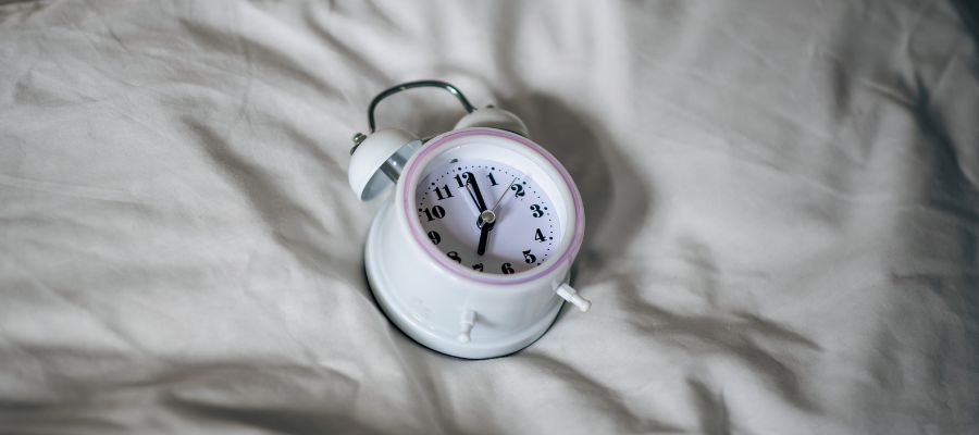White small alarm clock with a pink rim, on white linen symbolising circadian rhythm and sleep-wake cycle