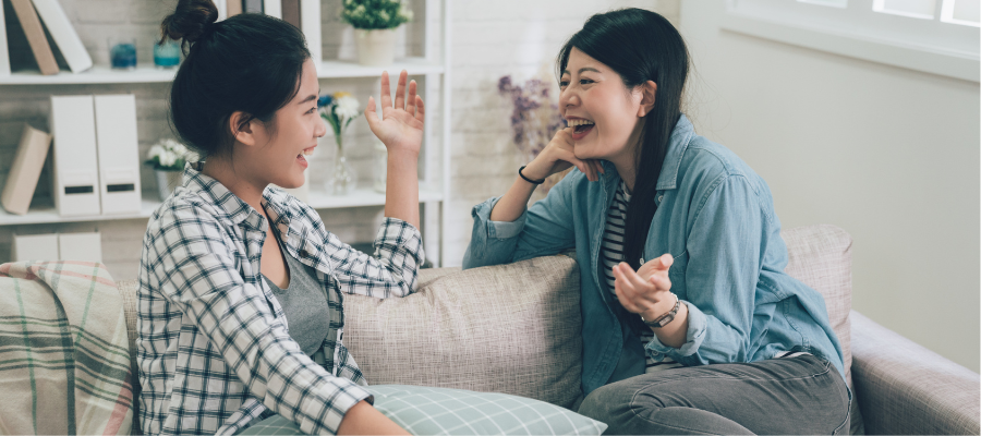 friends talking and laughing on a sofa with black hair and a book shelf in the background