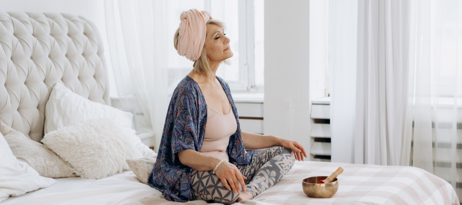 Middle aged woman sat cross legged on bed with headscarf meditating and relaxing