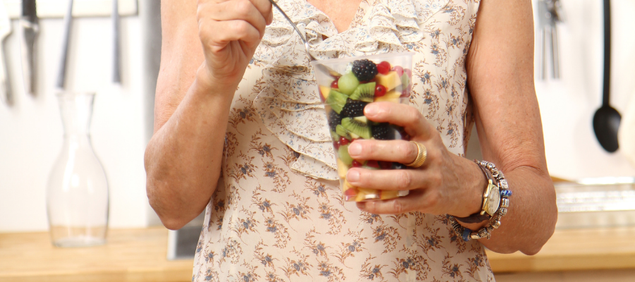 woman holding a glass of fruits including kiwis, pineapples and blackberries