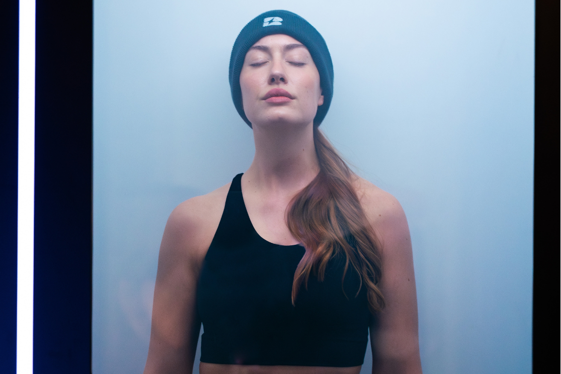 biowell health cryotherapy chamber with young woman in black outfit and woollen hat