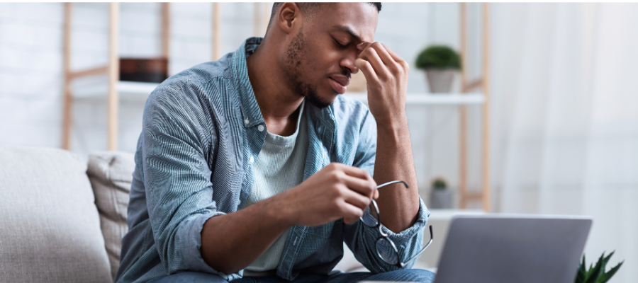 man wearing blue shirt sitting on a sofa in his living room looking tired and fatigued