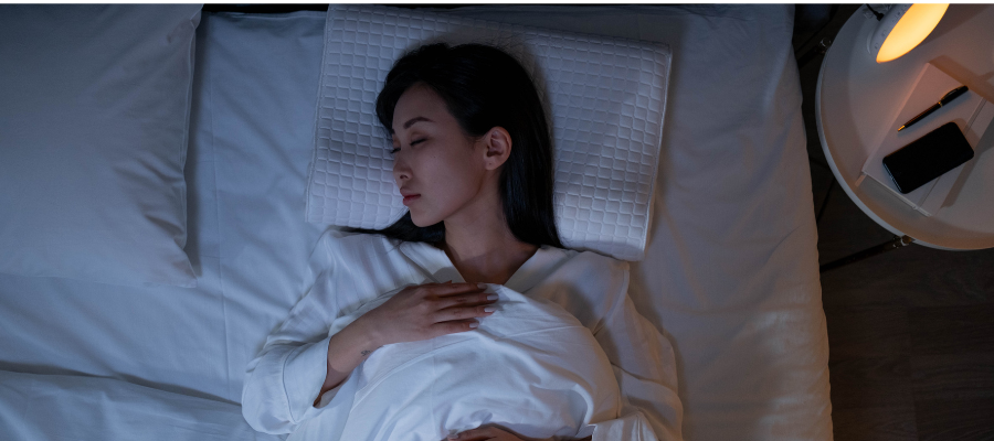 woman asleep in bed with low lighting and white bed sheets