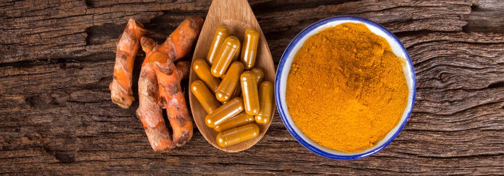 Curcumin root, tablets/capsules on a spoon, and powder in a jar on a wooden background