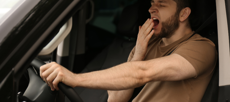 man yawning and tired whilst driving wearing a brown top