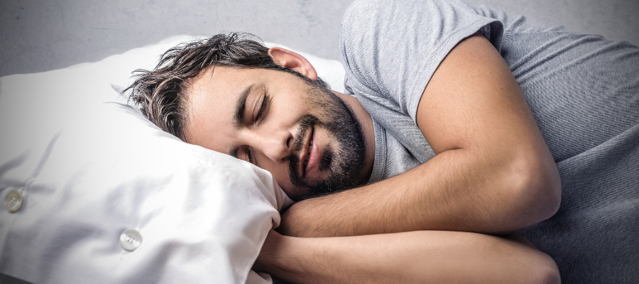 man lying down and sleeping with smile on his face and grey t shirt and white bedding