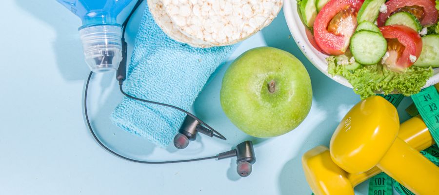 Healthy lifestyle showing gym gear, gym weights, rice cakes, green apple, bowl of salad, headphones, towel and tape measure