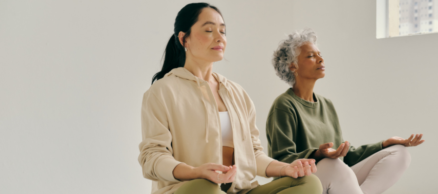 Two women meditating together in a calm cream space, with eyes closed