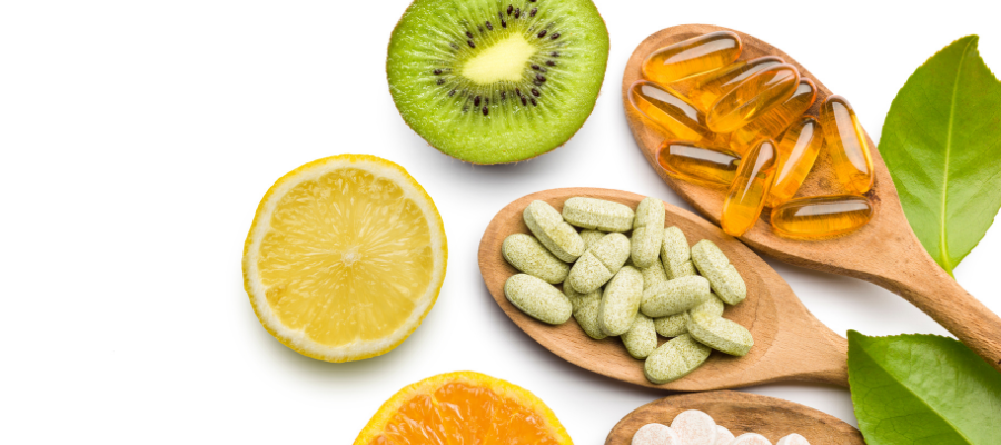 wooden spoons with supplements on and fresh fruits oranges and kiwis
