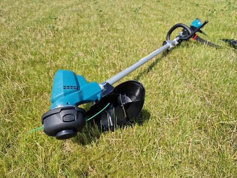 Battery powered electric grass trimmer laying on the cut lawn