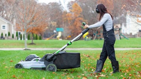 A woman uses the push lawn mower with the attached grass-clipping bag to it