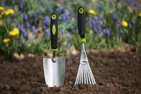 Garden tools like a hand trowel and a rake in garden soil