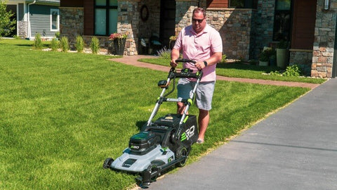 A middle - adged man mowing the lawn with the push lawn mower and the Trimyxs attachment