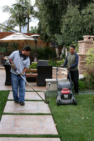 A man edging a lawn. Another man mowing the lawn with the push lawn mower