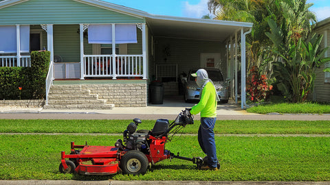 A worker uses a big red push lawn mower to mow front yard of a house