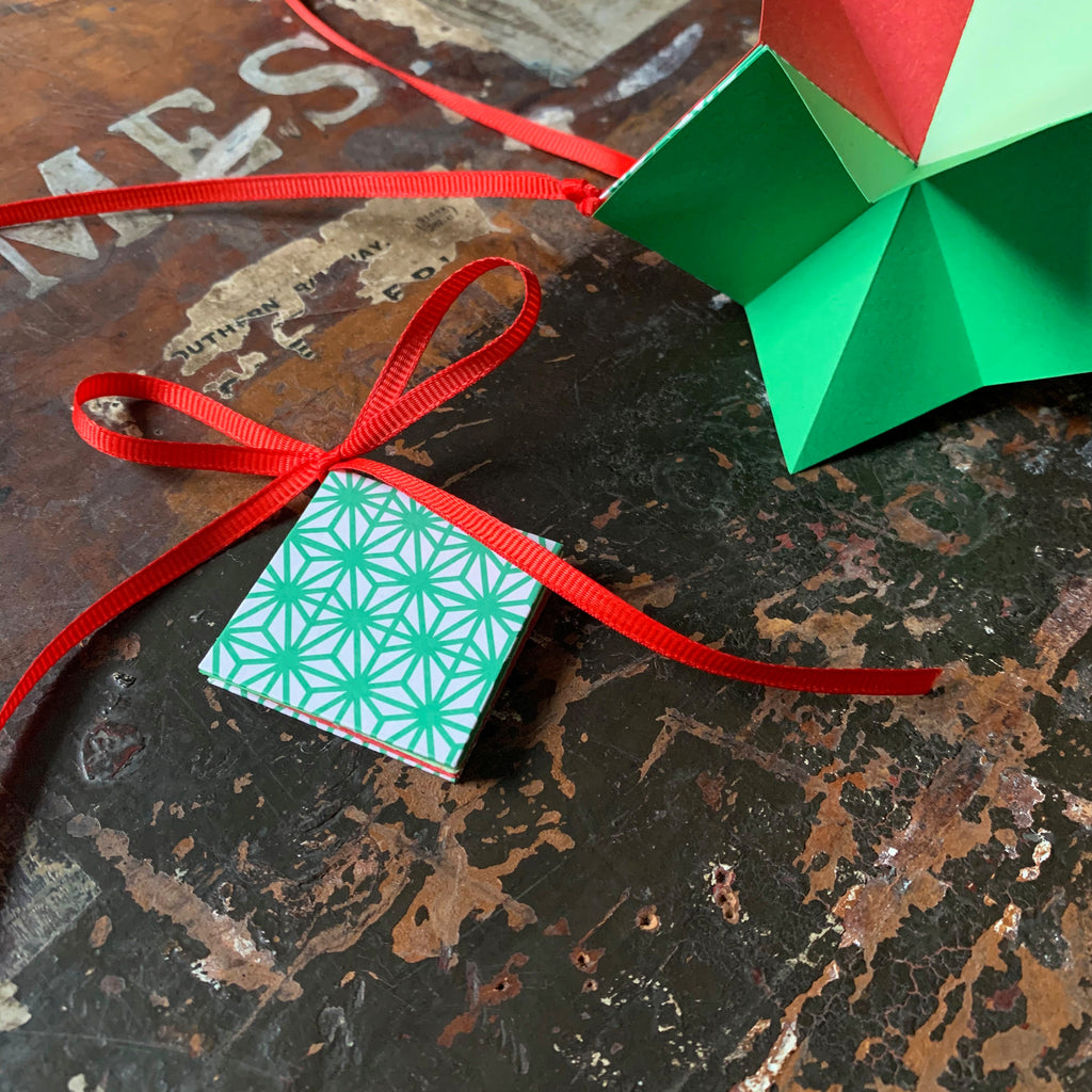 The origami star book tied shut with a ribbon bow, and tied open ready for hanging.