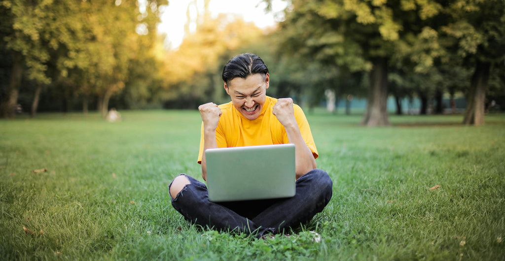 Happy guy stting on a park grass with a laptop