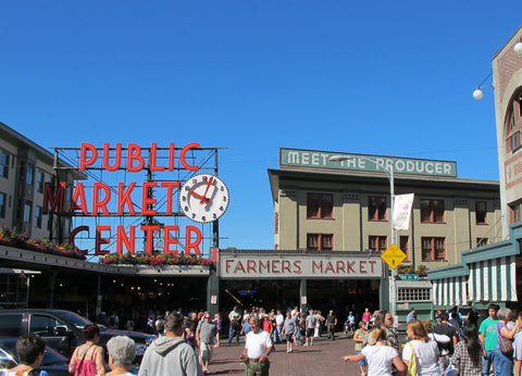 busy city farmers market with large red neon sign and clock