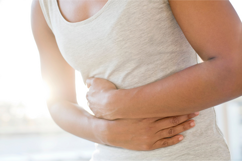 Person ins gray tank top holding stomach from IBS stomach pain