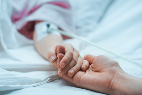 Person in hospital bed holding hands