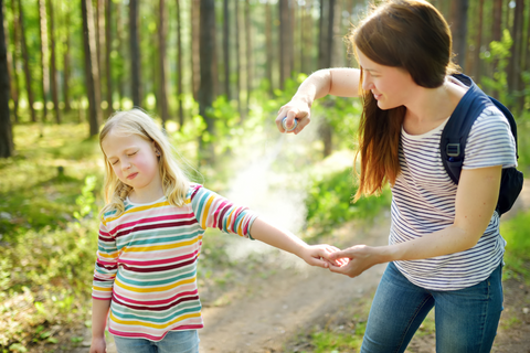 Woman spraying bug spray on child in the woods