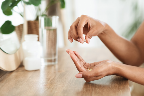 Person holding zinc pills in hand next to glass of water on table