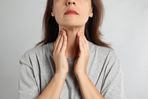 Woman in gray shirt holding throat near thyroid gland