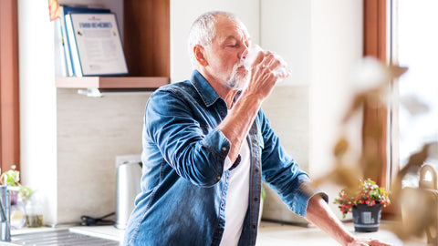older man drinking water in kitchen