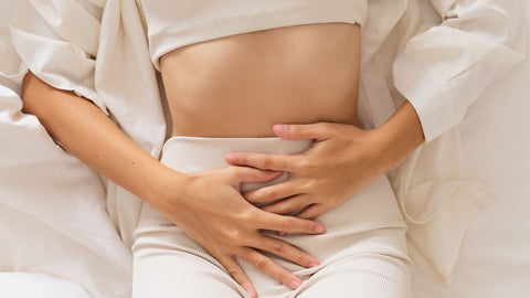 Woman in tan leggings holding pelvis with endometriosis symptoms