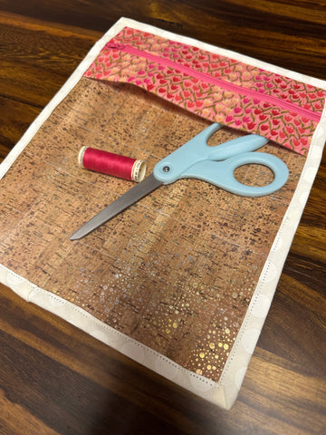 Photo of completed cork project bag with a white binding attached and a spool of thread and pair of scissors in the bag