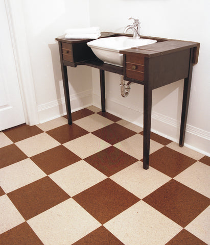 A sink set in an old vanity on a checkered cork flooring that is brown and white.