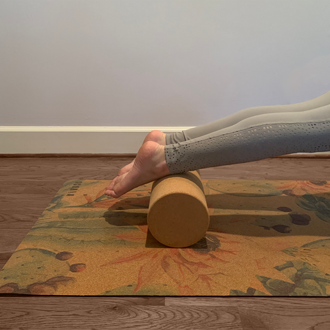 A woman using a cork yoga roller under her calves while doing pushups.