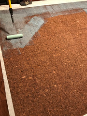 Contact cement being rolled onto the back of glue down cork flooring tiles.