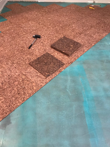 Glue down cork flooring tiles being applied to subfloor after contact cement has dried