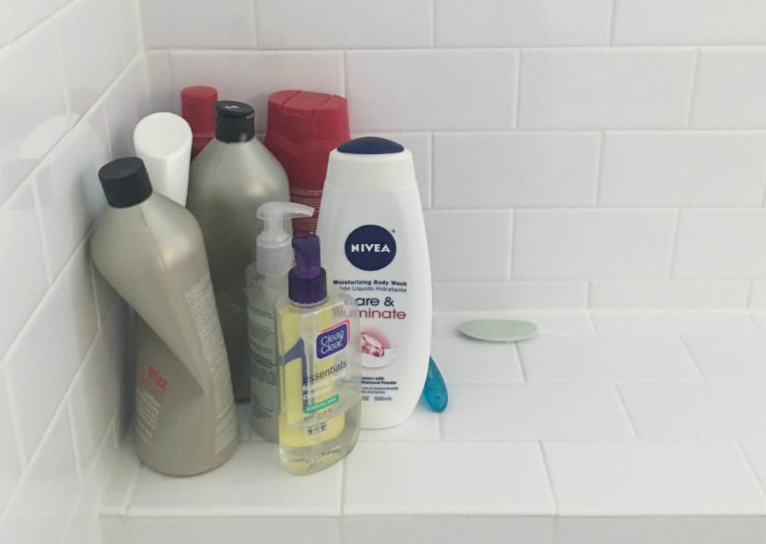 Shampoo, body wash, and soap bottles arranged on a white tiled shower shelf.