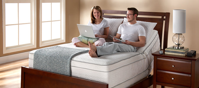 A couple sitting on an adjustable bed smiling