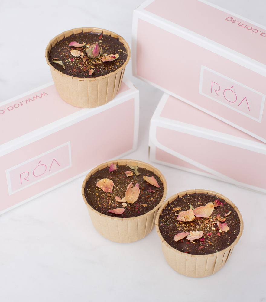 
                  
                    Load image into Gallery viewer, 3 chocolate cupcakes covered with a dark chocolate ganache and sprinkled with edible gold flakes and Moroccan rose buds with pink and also with white packaging boxes by side
                  
                