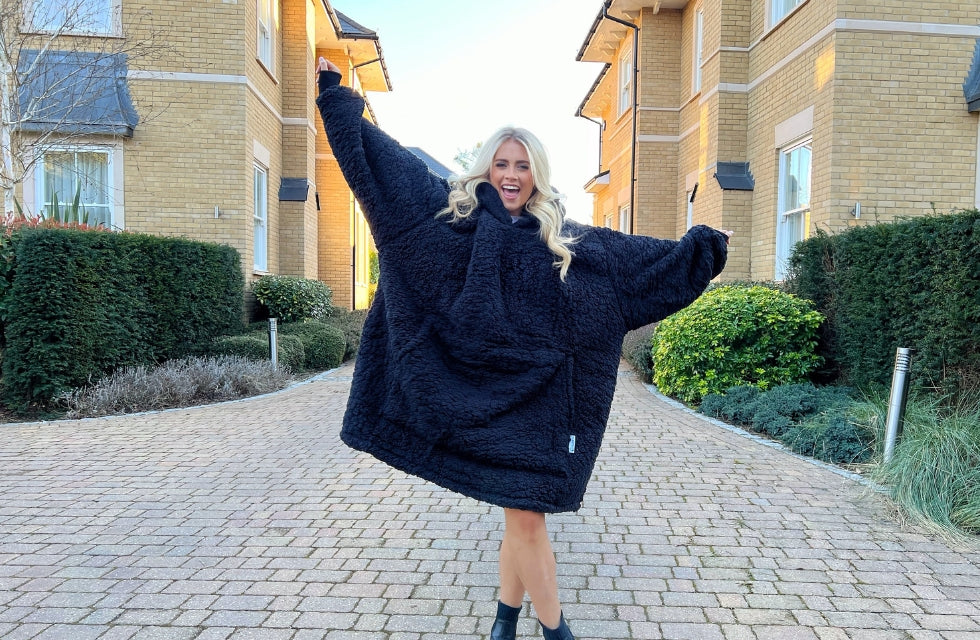 Woman wearing hoodie blanket outdoors with arms in the air