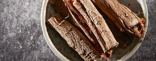 A bowl containing several pieces of dried bark on a textured surface.