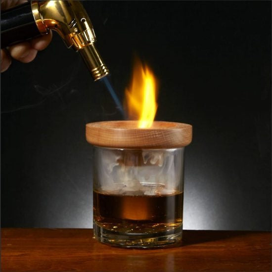 Torch lighting a smoker kit on top of whiskey glass