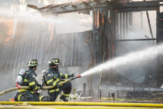 Two firefighters hosing down a building